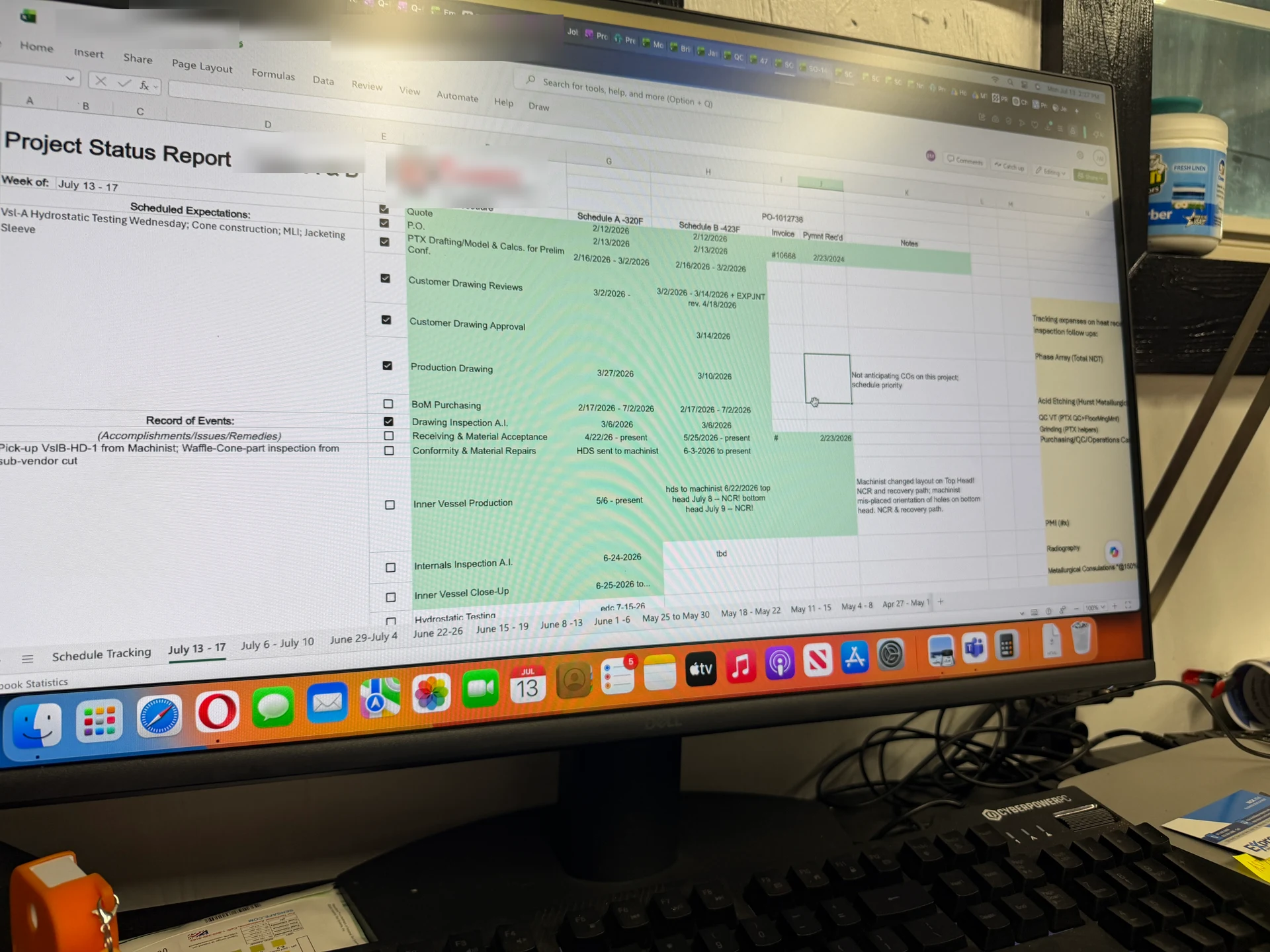 A photograph of a partner facility shop floor monitor running the legacy project status report as a colour-coded Excel workbook
