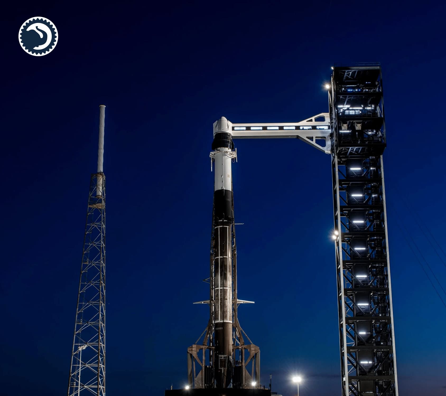 A launch vehicle stacked on the pad at dusk, crew access arm extended from the tower